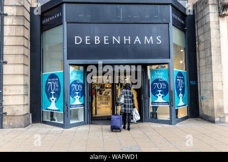 Retro della signora shopper borse e zaini e wheeling una borsa da viaggio di entrare in un negozio Debenhams con grande croce blu vendita segni nel windows Princes Street Foto Stock