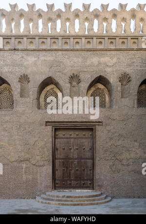 Invecchiato in legno porta a spiovente, arcuata forata finestra di stucco decorato con motivi floreali e tre passaggi su pietra muro in mattoni, Ibn Tulun moschea, Il Cairo, Egitto Foto Stock