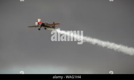 Aeroplano facendo acrobazie aeree con emissione di fumo bianco sentieri in un cielo grigio Foto Stock