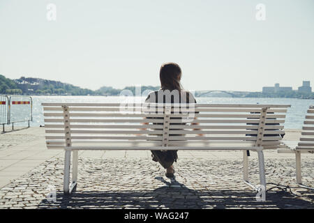 La ragazza si siede su una panchina lungo il fiume e enjoysscenic vista del fiume in una giornata di sole. Foto Stock