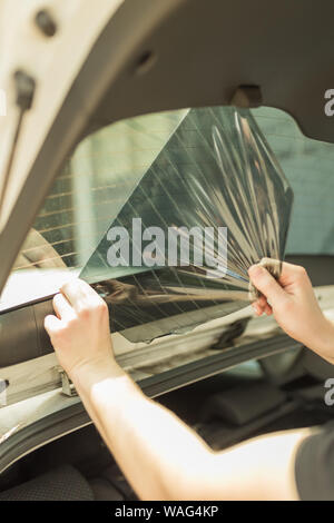 Lavoratore rimozione auto vecchia finestra di protezione in vetro tint lamina dalla finestra del trunk. Foto Stock