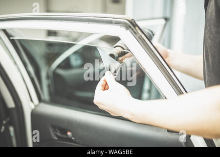 Lavoratore rimozione auto finestra foglio di pellicola utilizzando la pistola ad aria calda. Foto Stock