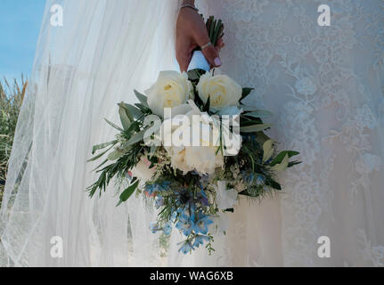 Sposa in piedi nel suo pizzo abiti da sposa tenendo le sue bouque di fiori Foto Stock