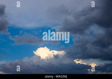 Azzurro cielo attraverso contrastanti nuvole pesanti. Il sole cade sulle nubi dopo un temporale. Bright bold texture di thunderclouds e cielo blu Foto Stock