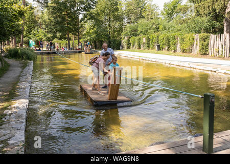 Visitatori godendo una giornata fuori a Kittenberger Erlebnisgärten tirando stessi attraverso un laghetto con un traghetto via cavo Foto Stock