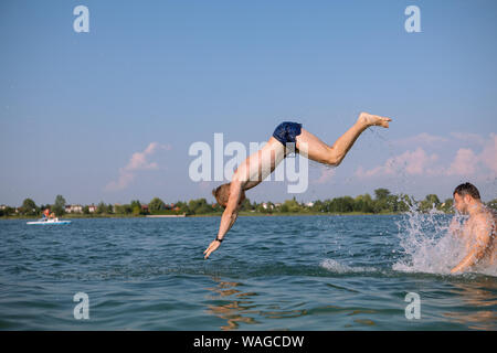 Coppia di maschi amici divertendosi nel lago saltando da spalle Foto Stock