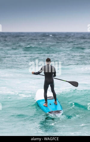 Un stand up paddle boarder voce fuori in mare a Fistral a Newquay in Cornovaglia. Foto Stock