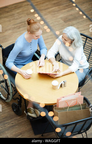 Madre e figlia utilizzando un tablet pc e discutere di qualcosa durante il riposo in cafe dopo lo shopping Foto Stock
