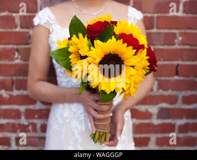 Sposa con bridal bouquet di girasoli e rose rosse, focus sui fiori. Foto Stock