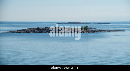 Estate scandinava in arcipelago toscano - molto bassi isolotti oblunga passando da acque blu del Mar Baltico. Cespugli verdi crescente dalle rocce, minuscoli uomini Foto Stock