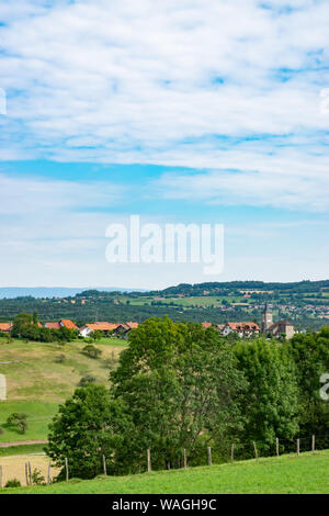 Collinare e pittoresca vista del paesaggio di prati, pascoli e campi, alberi, città di Brens e nuvole bianche nel cielo blu. Foto Stock