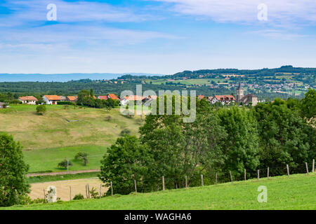 Collinare e pittoresca vista del paesaggio di prati, pascoli e campi, alberi, città di Brens e nuvole bianche nel cielo blu. Foto Stock