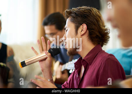 Giovani asiatici uomini adulti rock band membri ripassando cantare suonare strumenti musicali nel salotto di una casa Foto Stock