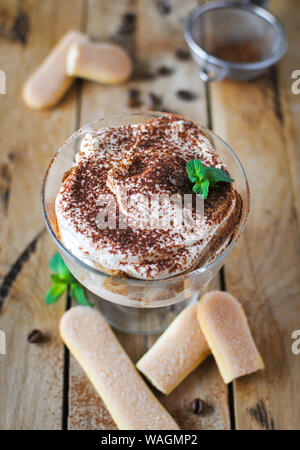 Tiramisù classica torta in un bicchiere con la menta fresca, su sfondo di legno Foto Stock