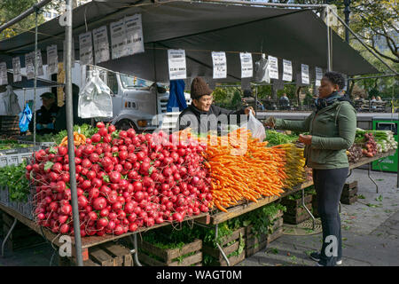 Un americano asiatico uomo vendita di produrre per un africano donna americana a lui Union Square Mercato verde a Manhattan, New York City. Foto Stock
