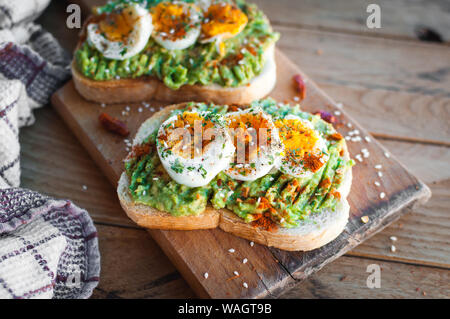 Close-up di avocado uova e pane tostato con erbe aromatiche e spezie, sul bordo di taglio Foto Stock