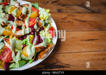 Close-up di insalata di pollo con verdure fresche in una piastra e avocado dressing, su sfondo di legno Foto Stock