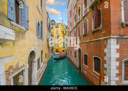 Un gondoliere manzi una gondola riempito con i turisti in un piccolo e stretto, verde smeraldo di canale e su una soleggiata giornata estiva a Venezia, Italia Foto Stock
