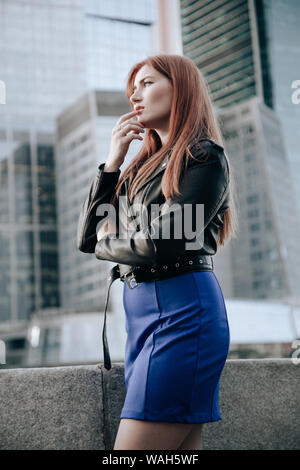 Taglie donna con i capelli rossi che indossa vestito blu e cuoio giacca nera Foto Stock