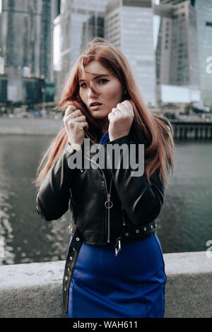 Taglie donna con i capelli rossi che indossa vestito blu e cuoio giacca nera Foto Stock