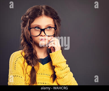 Pensiero serio smorfie schoolgirl in occhiali cercando su grigio di sfondo per studio. Si torna a scuola. Il concetto di istruzione. Closeup tonica vina Foto Stock