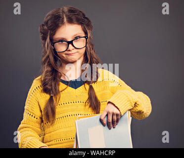 Pensiero serio smorfie schoolgirl in occhiali azienda libri di esercizi su grigio di sfondo per studio. Si torna a scuola. Il concetto di istruzione. Chiudere Foto Stock