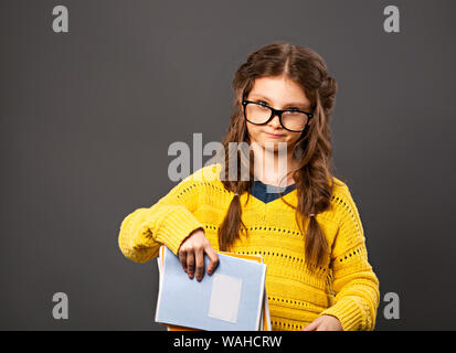 Pensiero serio smorfie schoolgirl in occhiali azienda libri di esercizi su grigio di sfondo per studio. Si torna a scuola. Il concetto di istruzione. Chiudere Foto Stock