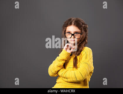 Pensiero serio smorfie schoolgirl in occhiali cercando su grigio di sfondo per studio. Si torna a scuola. Il concetto di istruzione. Closeup ritratto Foto Stock