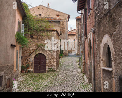 Una pietra di strette strade lastricate e vecchie case medievali con arcate di porte in legno anche metallo tende alle finestre in cittadina antica Sermoneta, Italia Foto Stock