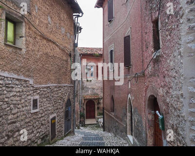 Una pietra di strette strade lastricate e vecchie case medievali con arcate di porte in legno anche metallo tende alle finestre in cittadina antica Sermoneta, Italia Foto Stock