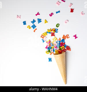 Piccole casette di legno policroma lettere dell'alfabeto inglese diffusa da una superficie conica waffle cup, sfondo bianco, vista dall'alto Foto Stock