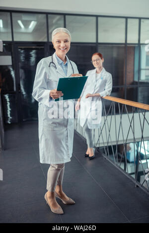 Felice femmina senior medico in camice bianco Foto Stock