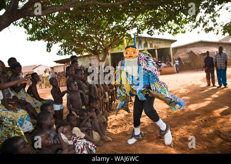 Africa occidentale Benin. Maschera Gelede ballerina avvicinando il gruppo di affascinare i bambini. Foto Stock