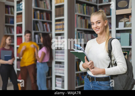 Intelligent giovane ragazza sorridente su sfondo della libreria Foto Stock