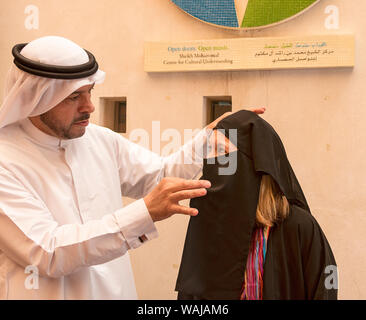 Dubai, EAU. Guida in un tradizionale tunica araba e copricapo, aiuta a visitare donna americana provare sulla tradizionale abaya robe al Sheikh Mohammed Centro per la comprensione culturale. (MR, PR) Foto Stock