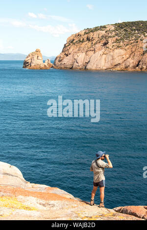 Australia e Tasmania, Maria Island. Escursionista visualizzazione dal bordo della scogliera di roccia Haunted Bay. (MR) Foto Stock