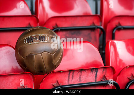 In pelle di antiquariato football soccer ball contro uno sfondo di sporco sedie rosse in un piccolo stadium Foto Stock