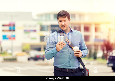 Sorridente uomo maturo utilizzando il telefono cellulare mentre si cammina sulla strada per andare al lavoro - Happy spensierata maschio freelance di bere il caffè mentre l'invio di messaggi Foto Stock