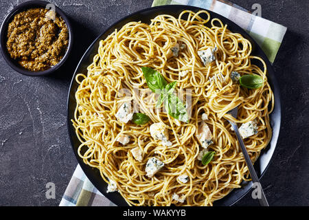 Close-up di spaghetti con basilico genovese pesto e formaggio blu su una piastra nera su una tavola di cemento, vista da sopra, flatlay, spazio di copia Foto Stock