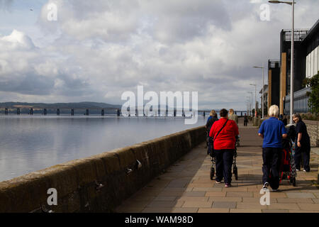 Dundee, Tayside, Scozia, Regno Unito, 21 Agosto, 2019. Regno Unito meteo: un giorno nuvoloso con alcuni incantesimi soleggiato, temperatura massima 19°C. Un giorno fuori per alcuni turisti in carrozzina sulla città di Dundee waterfront ammirando la vista della calma argenteo fiume Tay con 1800 famoso Tay ponte ferroviario in distanza. Credito: Dundee fotografico / Alamy Live News Foto Stock