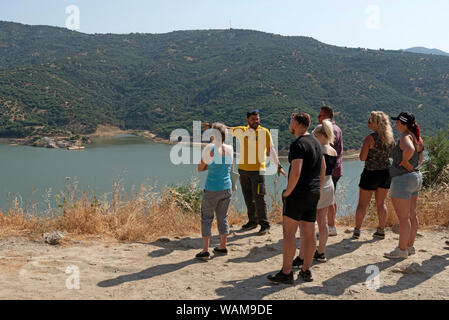 Creta, Grecia. Tour Guide in maglietta gialla sottolineando il villaggio sommerso di Sfentyi in corrispondenza del bordo della diga Aposelemis nel centro di Creta. Foto Stock