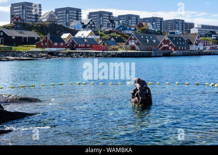 Scultura di Sedna, dea Inuit del mare circondato da acqua di mare nel porto coloniale (Kolonihavnen) con appartamenti moderni dietro. Nuuk Groenlandia Foto Stock