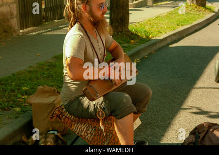 Cesis, Lettonia - Luglio 19, 2019: musicista di strada giocando il salterio mentre è seduto con un cane per strada in una giornata di sole. Foto Stock