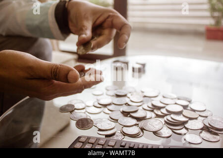 Immagine ritagliata di imprenditore contare monete utilizzando la calcolatrice a scrivania in ufficio. Commercianti lato contare monete. Finanza aziendale e risparmio Inves Foto Stock