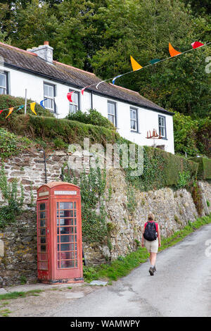 Gli escursionisti a piedi passato cottage bianco e un tradizionale telefono rosso scatola in lavaggio, Cornwall, Inghilterra. Foto Stock