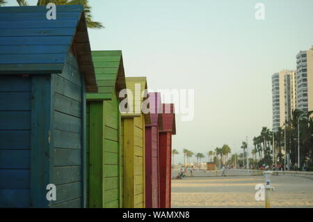 La spiaggia è colorata e si erge sulla sabbia, e grandi edifici sullo sfondo. Capanne colorate sulla spiaggia in Spagna Foto Stock