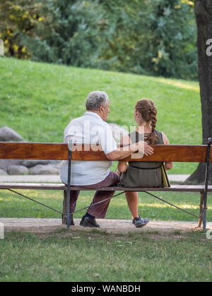 Il nonno e la sua nipote sta parlando e trascorrere del tempo insieme. Essi sono qui seduti sulla panchina del parco. Concetto intergenerazionale. Foto Stock