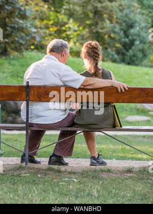 Il nonno e la sua nipote sta parlando e trascorrere del tempo insieme. Essi sono qui seduti sulla panchina del parco. Concetto intergenerazionale. Foto Stock