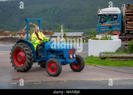 L'uomo giacca gialla la Guida 1963 Vintage Rosso Blu Fordson Super Dexta maschio del trattore impermeabili fluorescenti fuorigioco anteriore lato guida Loch Santa Marina 1 Foto Stock