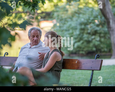 Il nonno e la sua nipote sta parlando e trascorrere del tempo insieme. Essi sono qui seduti sulla panchina del parco. Concetto intergenerazionale. Foto Stock